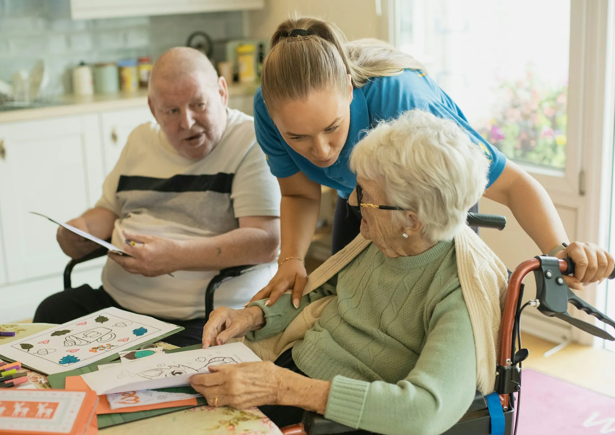 An aide standing with a group of older adults in a bright shared room