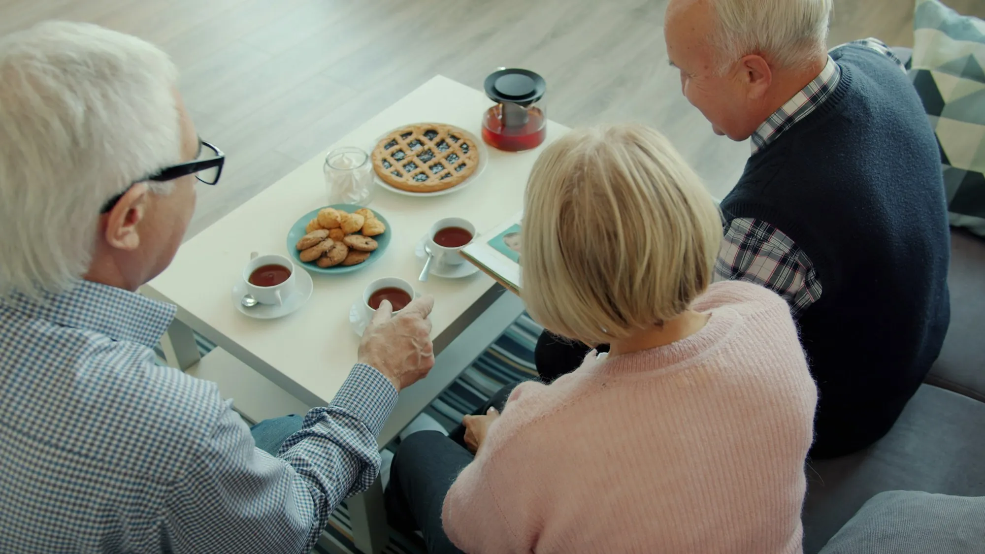 Three older adults looking through a photo album together over tea